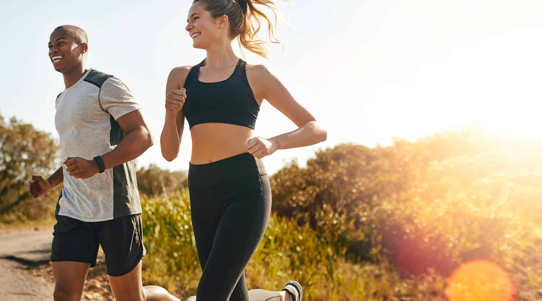 A man and woman jogging outdoors, enjoying a fitness session in the sunlight.