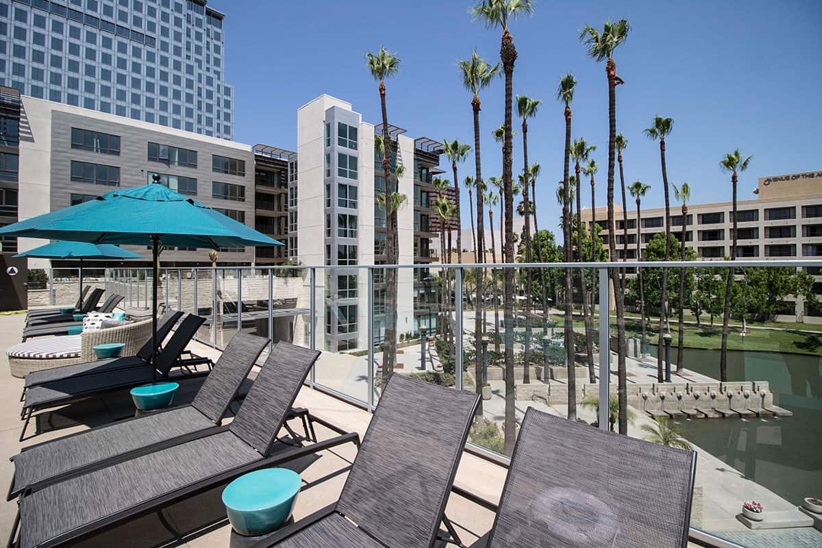 Outdoor lounging area with comfortable chairs and umbrellas, overlooking a peaceful water feature and lush palm trees.