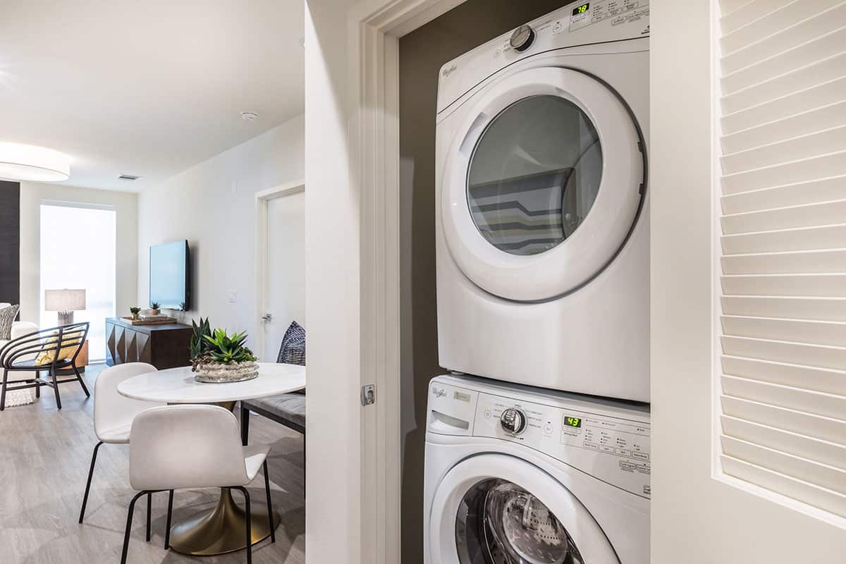 Closet with a washer and dryer setup, with the dining room and living room visible in the background, showcasing an integrated living space design.