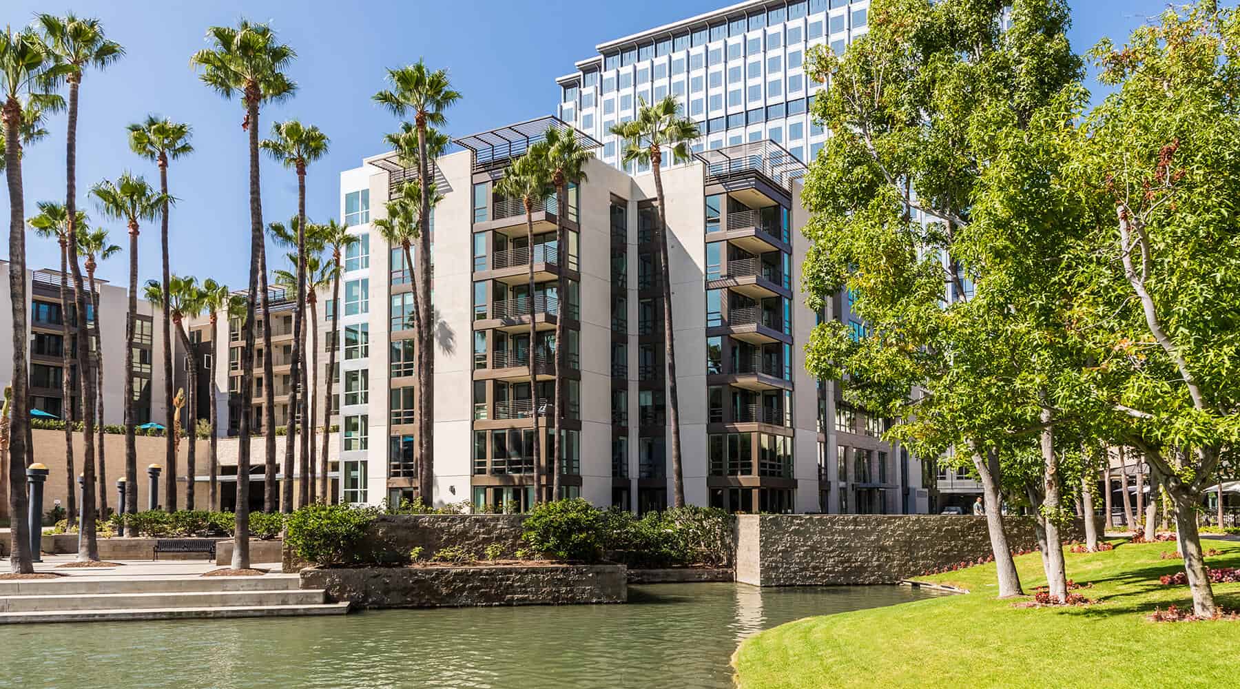 Building exterior with palm trees and a water feature in the foreground.