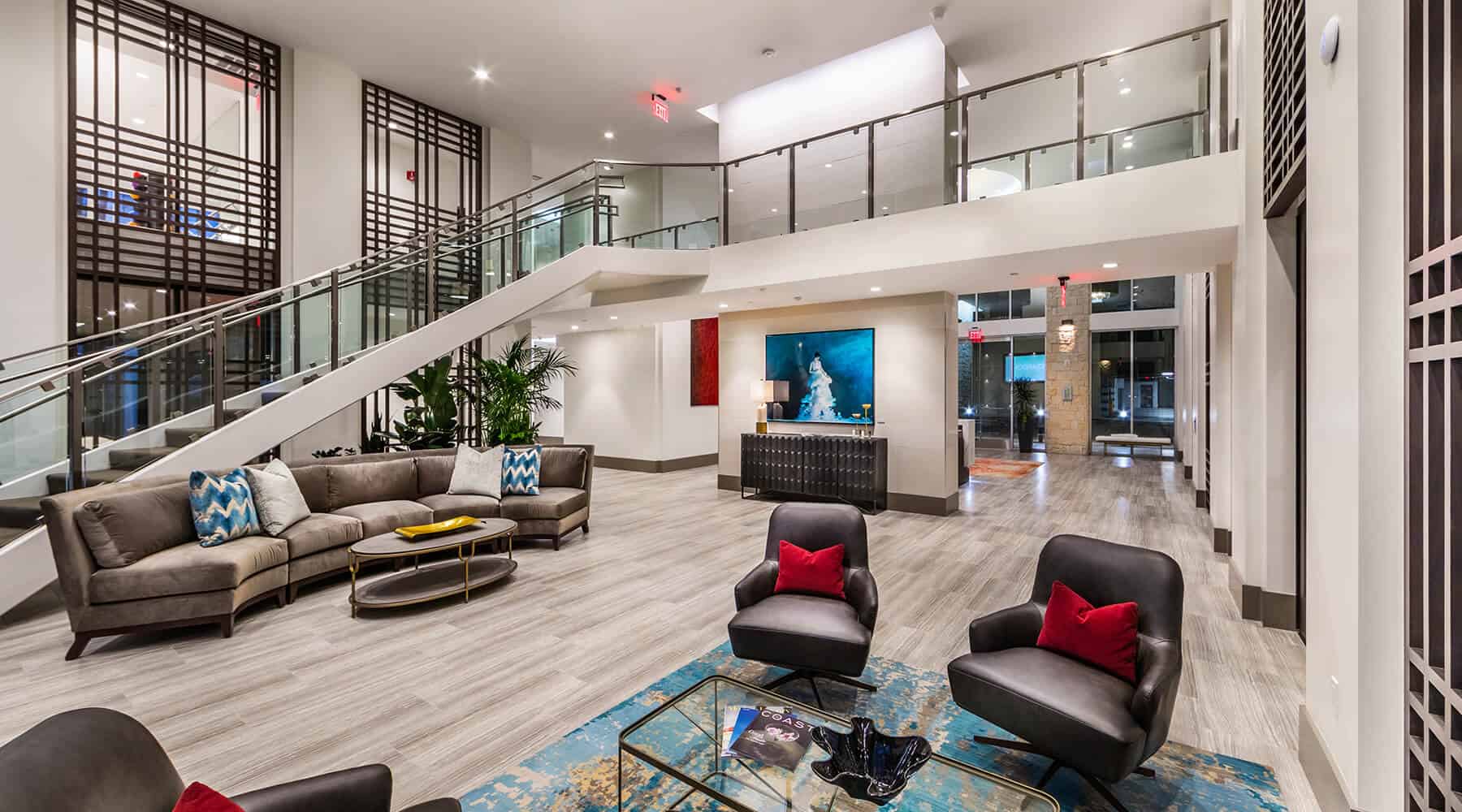 A modern lobby featuring a sectional sofa, armchairs, and contemporary artwork, with a staircase leading to the upper floor.
