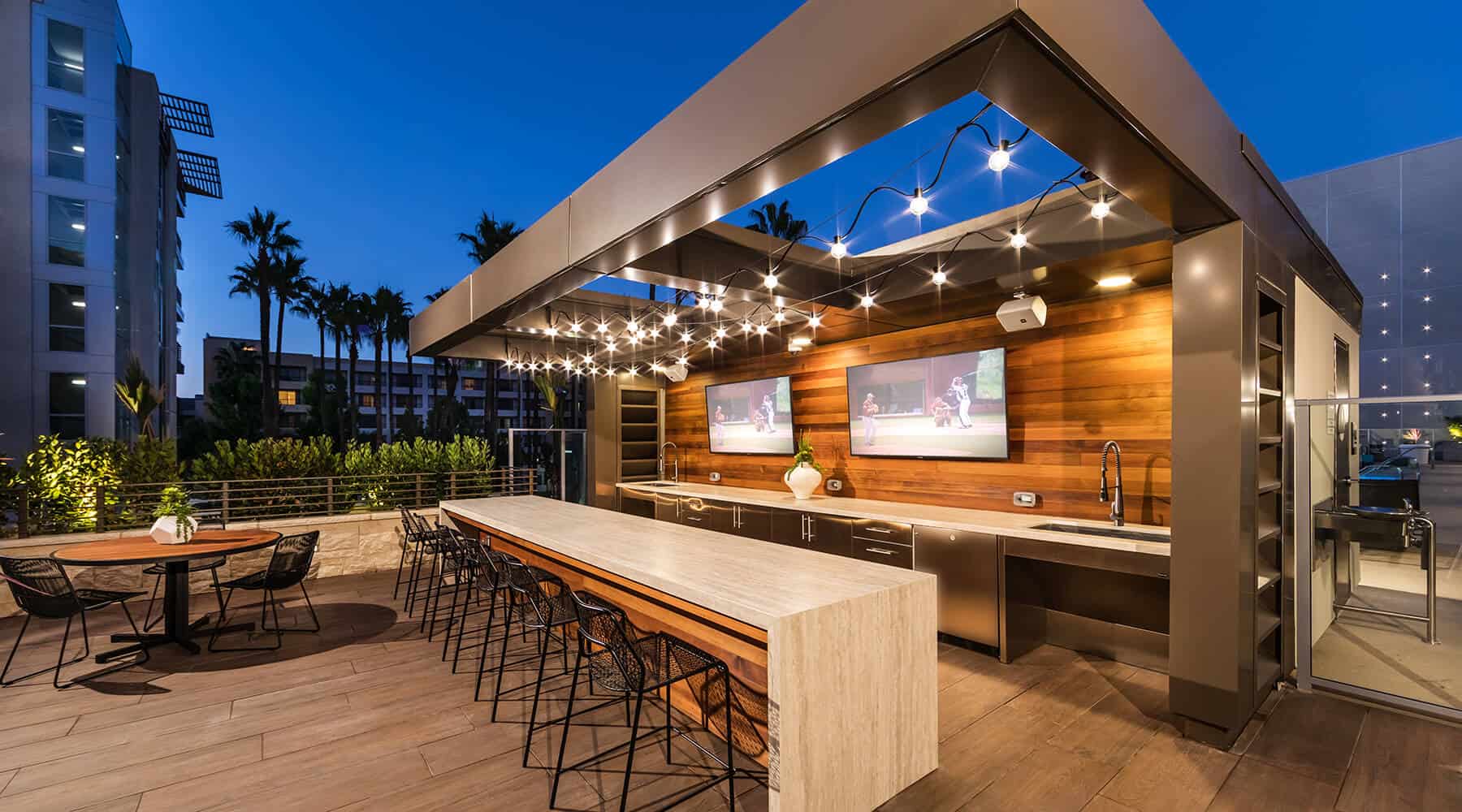 Outdoor kitchen at 580 Anton Apartments featuring a seating area, sink, and flat-screen TVs.