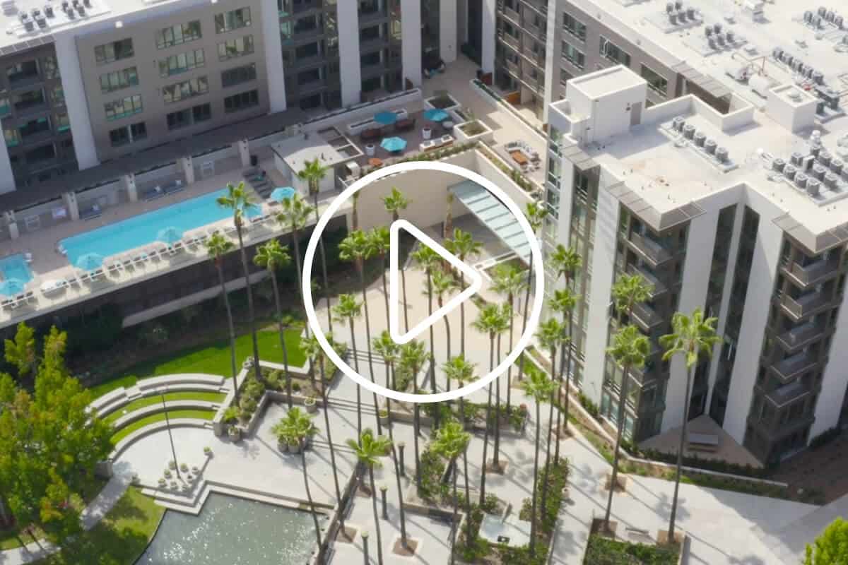 Aerial view of 580 Anton featuring the swimming pool, surrounding palm trees, and outdoor courtyard with a play button overlay for video content.